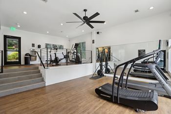 A gym with a treadmill, a staircase, and a ceiling fan.